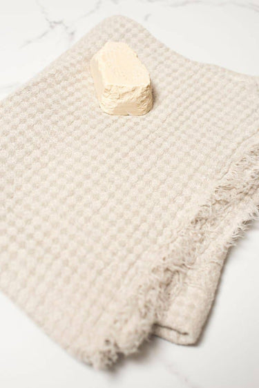 Beige textured wash cloth with a bar of soap on a white marble surface